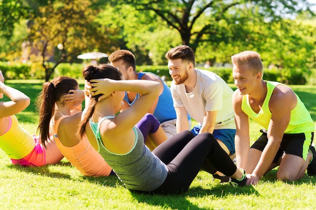 Concetto di fitness, sport, amicizia e stile di vita sano - gruppo di amici adolescenti felici o sportivi che si esercitano e fanno sit-up al campo di addestramento