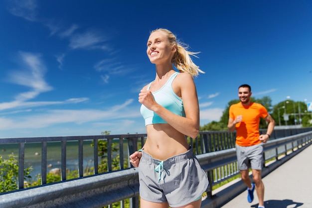 Fitness, sport, amicizia e concetto di stile di vita sano - coppia sorridente che corre al mare estivo