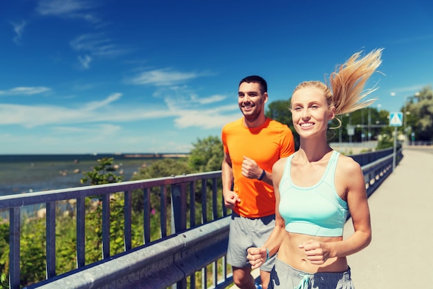 fitness, sport, friendship and healthy lifestyle concept - smiling couple running at summer seaside