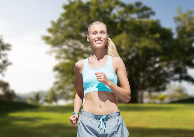 fitness, sport, friendship and healthy lifestyle concept - smiling young woman running or jogging over summer park background