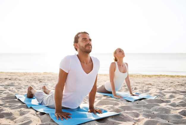 fitness, sport, friendship and lifestyle concept - couple making yoga exercises lying on mats outdoors