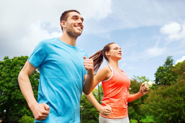 fitness, sport, friendship and lifestyle concept - smiling couple running outdoors