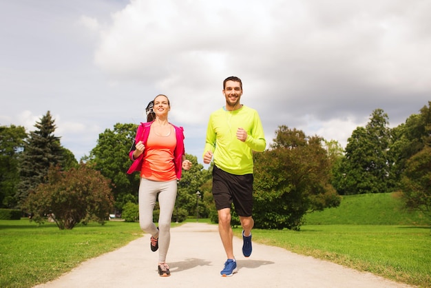 Fitness, sport, friendship and lifestyle concept - smiling\
couple with earphones running outdoors