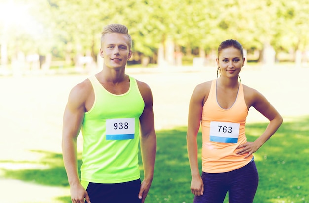 fitness, sport, friendship, marathon and healthy lifestyle concept - group of happy teenage friends or sportsmen couple with racing badge numbers outdoors