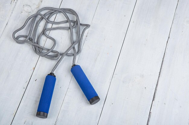 Photo fitness/sport and healthy lifestyle concept - jumping/skipping rope with blue handles on white wooden background