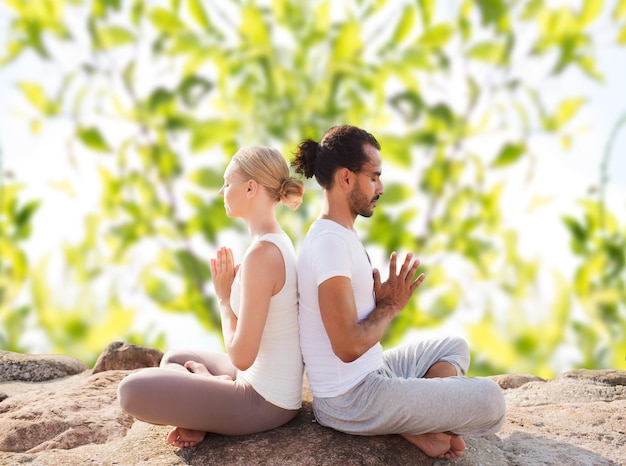 フィットネス、スポーツ、瞑想、ライフスタイルのコンセプト-屋外に座ってヨガの練習をする笑顔のカップル