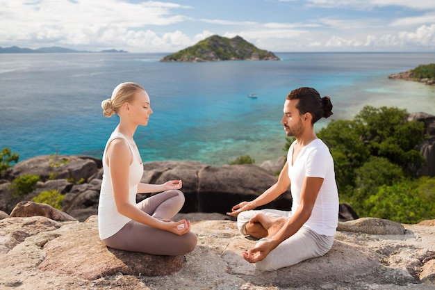 fitness, sport, meditation and people concept - happy couple doing yoga and meditating outdoors over natural background and sea