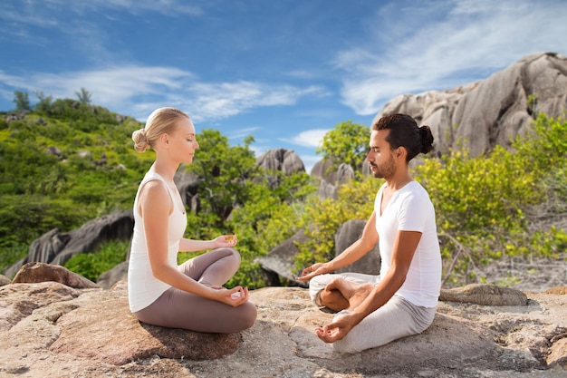 fitness, sport, meditation and people concept - happy couple doing yoga and meditating outdoors over natural background