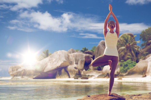 fitness, sport, mensen en een gezonde levensstijl concept - vrouw mediteren in yoga boom pose over exotische strand achtergrond van achteren