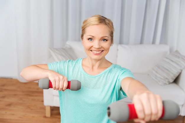 fitness, sport, mensen en gezond levensstijlconcept - glimlachende vrouw die thuis traint met halters op de mat