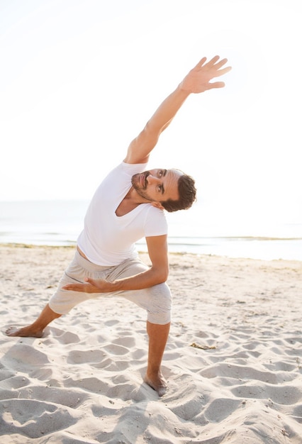 fitness, sport, mensen en lifestyle concept - glimlachende man die yoga-oefeningen maakt op het strand
