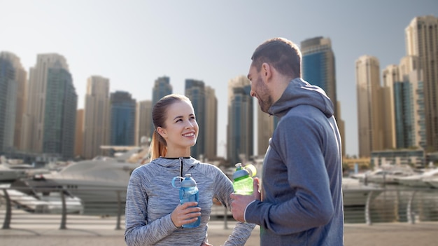 fitness, sport, mensen en lifestyle concept - lachend paar met flessen water buitenshuis over de straatachtergrond van de stad Dubai