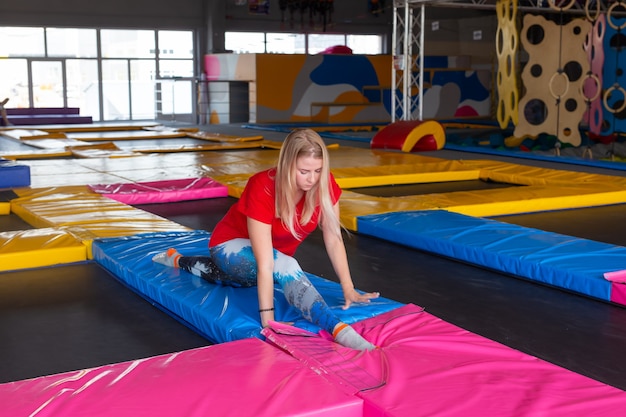 Fitness, sport, oefenen, stretching en mensenconcept - glimlachende vrouw die spagaat op mat over gymnastiekachtergrond doet.