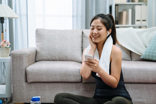 fitness sport opleiding technologie levensstijl concept. lachende vrouw met smartphone en bluetooth-koptelefoon geniet van muziek met een handdoek om de nek. vrolijke dame luister liedje in draadloze koptelefoon op yogamat