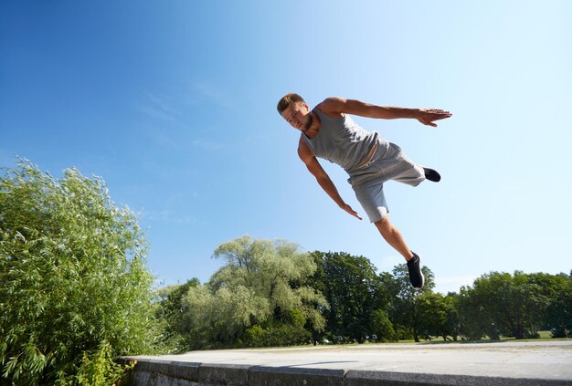 フィットネス、スポーツ、パルクール、人々 のコンセプト - 夏の公園でジャンプする若い男