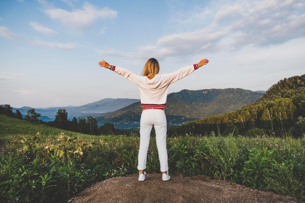 Fitness sport peope and emotions concept happy woman in sportswear enjoying freedom over mountains and blue sky background rear view on the back