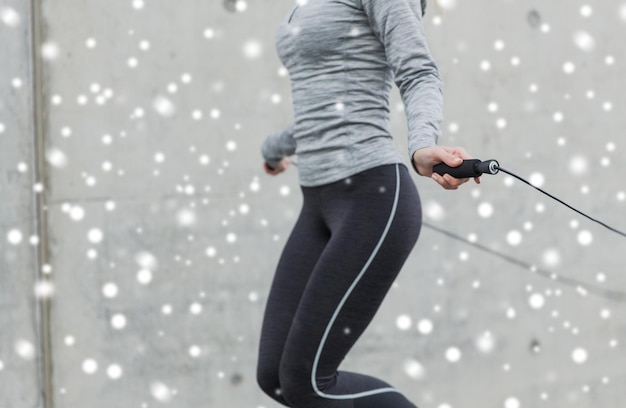 fitness, sport, people, exercising and healthy lifestyle concept - close up of woman skipping with jump rope outdoors over snow