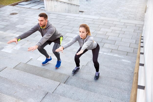 fitness, sport, people, exercising and lifestyle concept - couple doing squats on city street stairs