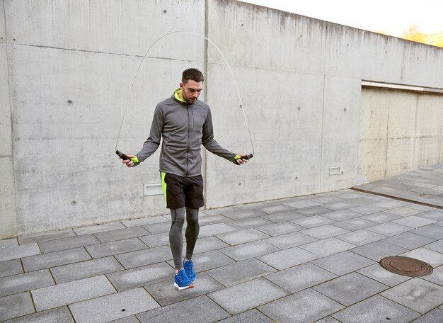 fitness, sport, people, exercising and lifestyle concept - man skipping with jump rope outdoors