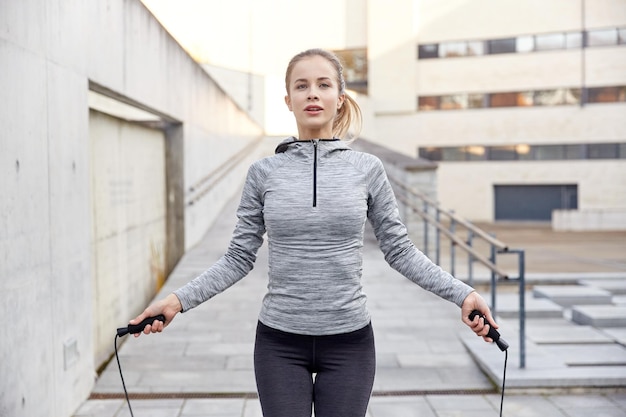 fitness, sport, people, exercising and lifestyle concept - woman skipping with jump rope outdoors