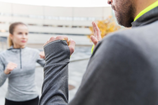 fitness, sport, people, exercising and martial arts concept - close up of woman with trainer working out self defense strike on city street