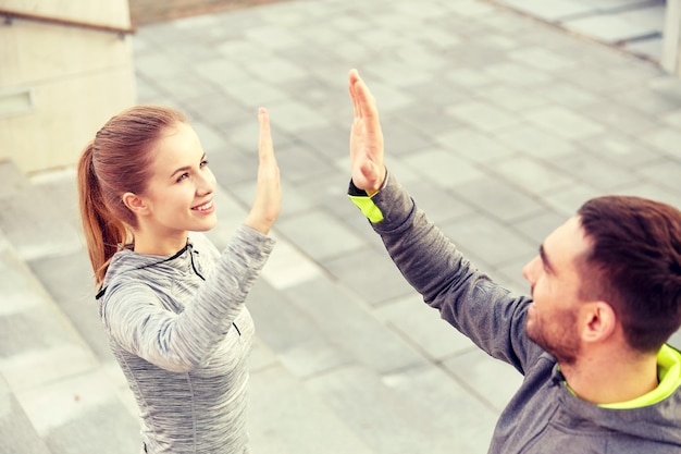 fitness, sport, people and gesture concept - smiling couple making high five on city street