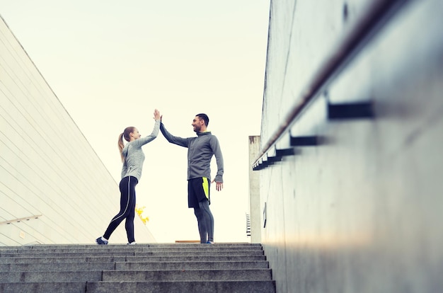 fitness, sport, people and gesture concept - smiling couple making high five on city street