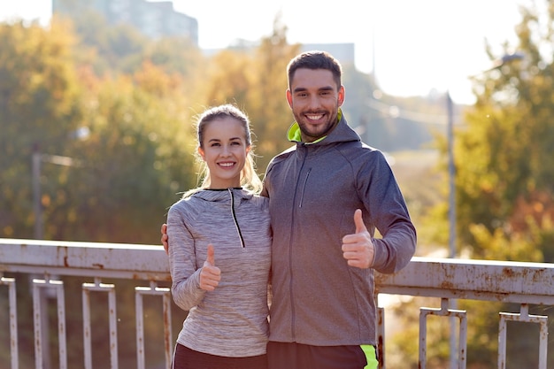 fitness, sport, people, gesture and lifestyle concept - smiling couple outdoors showing thumbs up at city