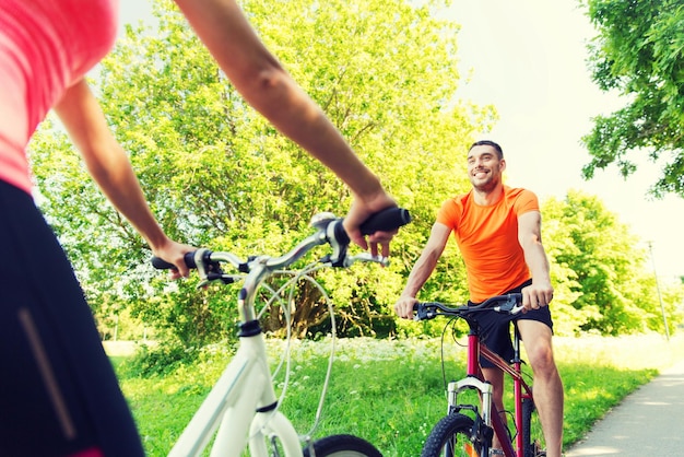 Foto fitness, sport, persone e concetto di stile di vita sano - primo piano di coppia felice in bicicletta all'aperto in estate