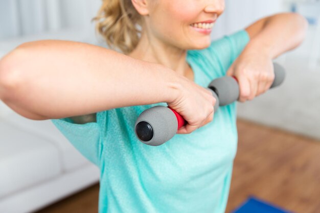 Photo fitness, sport, people and healthy lifestyle concept - close up of smiling woman exercising with dumbbells at home