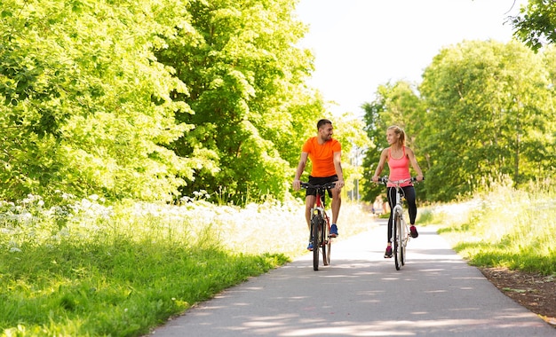фитнес, спорт, люди и концепция здорового образа жизни - счастливая пара катается на велосипеде на открытом воздухе летом