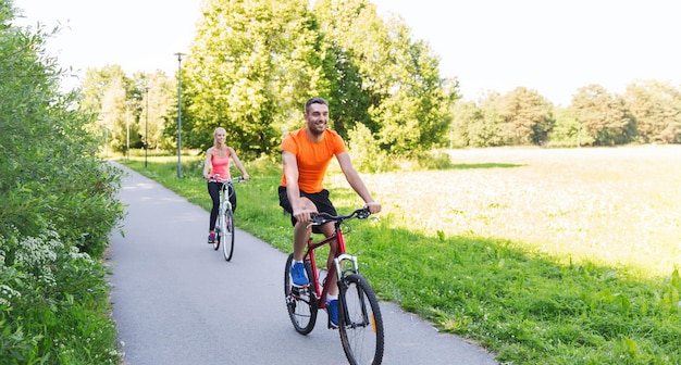 fitness, sport, people and healthy lifestyle concept - happy couple riding bicycle outdoors at summer