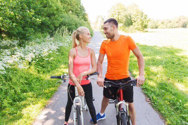 fitness, sport, people and healthy lifestyle concept - happy couple riding bicycle outdoors at summer