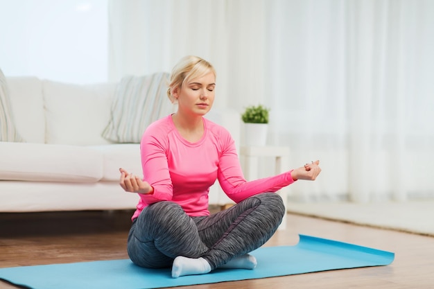 fitness, sport, people and healthy lifestyle concept - happy plus size woman stretching leg on mat at home