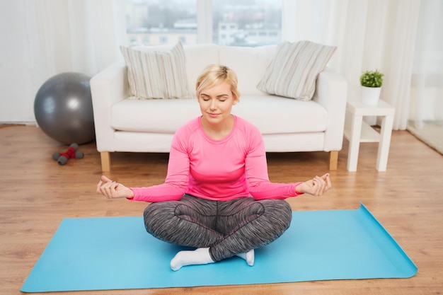 fitness, sport, people and healthy lifestyle concept - happy plus size woman stretching leg on mat at home