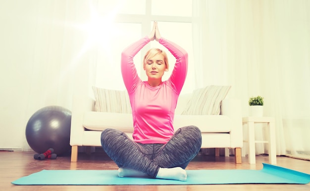 fitness, sport, people and healthy lifestyle concept - happy plus size woman stretching leg on mat at home