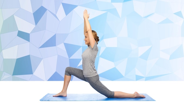 fitness, sport, people and healthy lifestyle concept - happy woman making yoga in low lunge pose on mat over blue polygonal background