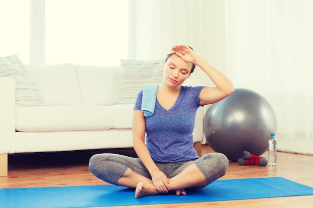 fitness, sport, people and healthy lifestyle concept - tired woman with towel after exercising on mat at home