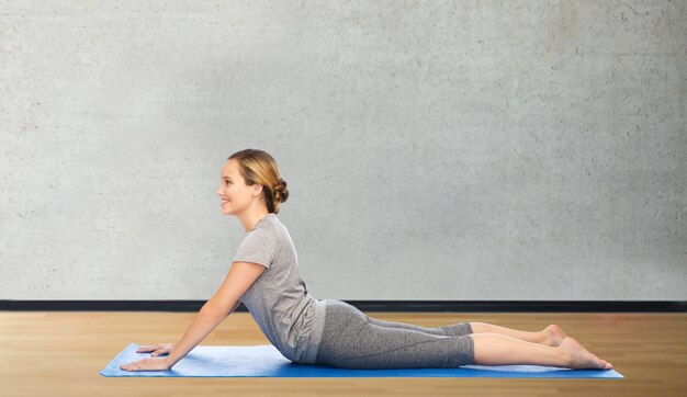 fitness, sport, people and healthy lifestyle concept - woman making yoga in dog pose on mat over room or gym background