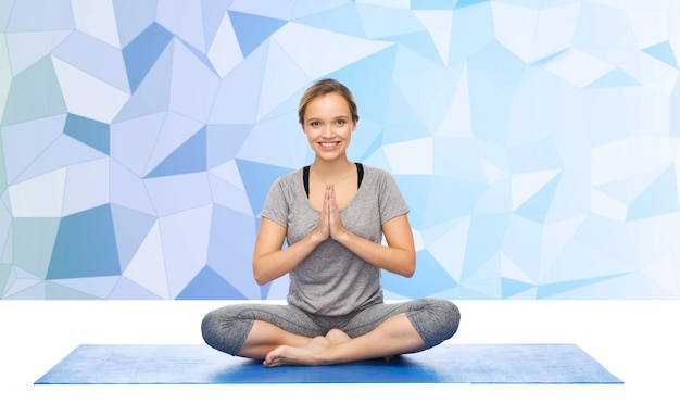 Photo fitness, sport, people and healthy lifestyle concept - woman making yoga meditation in lotus pose on mat over low poly background