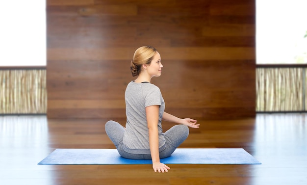 fitness, sport, people and healthy lifestyle concept - woman making yoga in twist pose on mat over wooden gym background