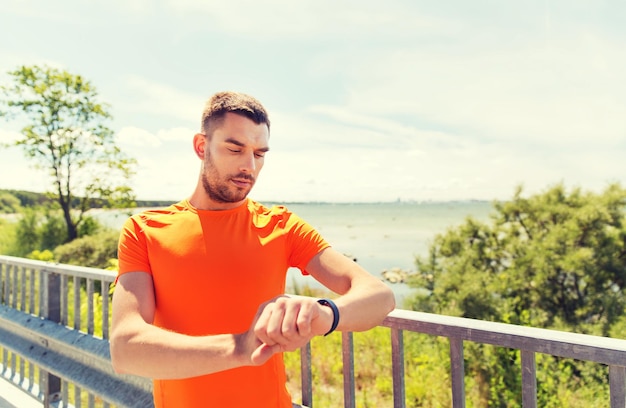 Fitness, sport, people and healthy lifestyle concept - young man with smart wristwatch at summer seaside