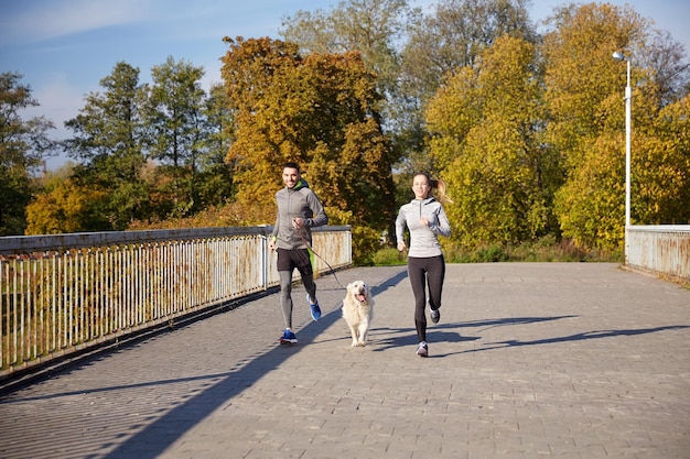 концепция фитнеса, спорта, людей и бега трусцой - счастливая пара с собакой, бегущей на улице