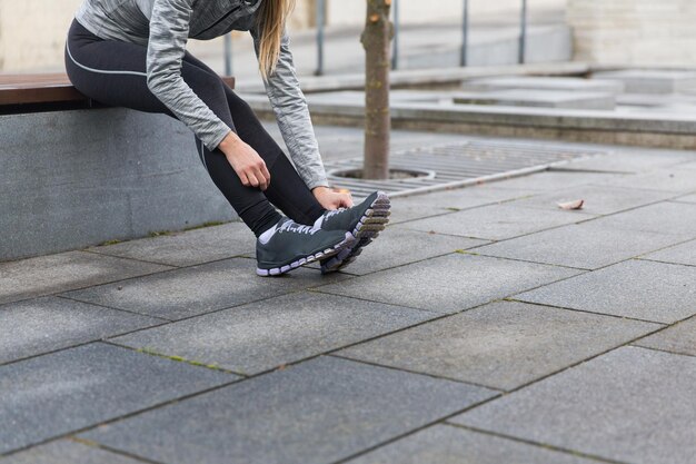 fitness, sport, people and lifestyle concept - close up of young sporty woman tying shoes outdoors