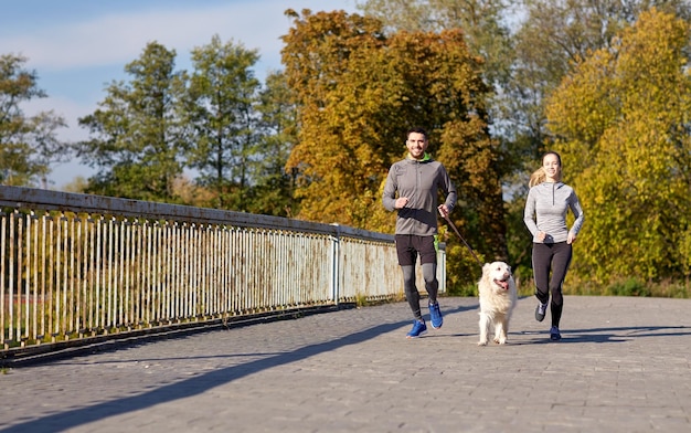 フィットネス、スポーツ、人々、ライフ スタイル コンセプト - 屋外を走っている犬と幸せなカップル