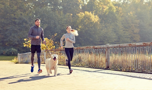 フィットネス、スポーツ、人々、ライフ スタイル コンセプト - 屋外を走っている犬と幸せなカップル