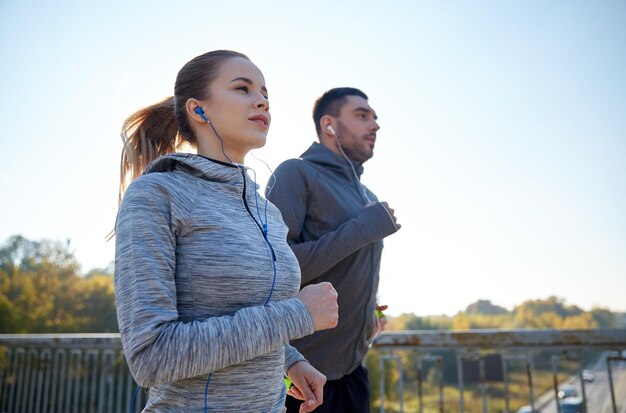 fitness, sport, people and lifestyle concept - happy couple with earphones running outdoors