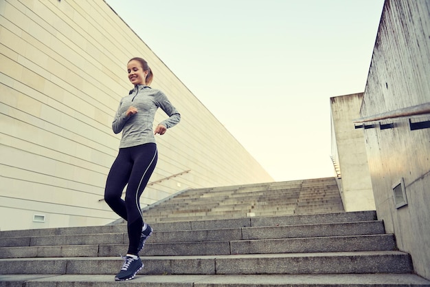 fitness, sport, people and lifestyle concept - happy sporty woman running downstairs in city