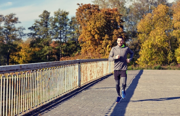 fitness, sport, people and lifestyle concept - happy young man running over city bridge