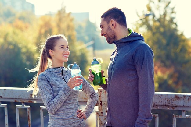フィットネス、スポーツ、人々、ライフ スタイル コンセプト - 屋外の水のボトルとカップルの笑顔